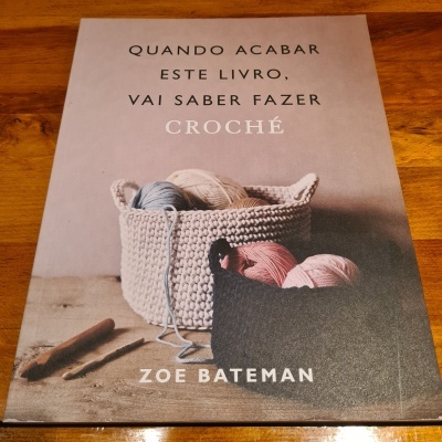 Capa de livro sobre crochê com cesto de crochê bege e novelos de lã coloridos