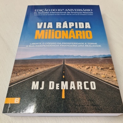 Capa do livro 'Via Rápida Milionário' com estrada deserta ao horizonte e texto em branco e laranja.