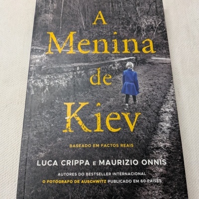Capa de livro A Menina de Kiev com criança de casaco azul de costas numa paisagem cinzenta