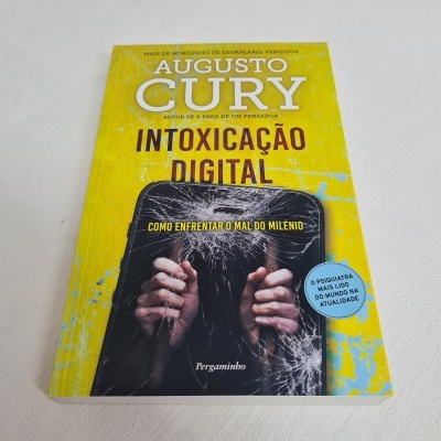 Livro com capa amarela e imagem de mãos segurando telemóvel rachado