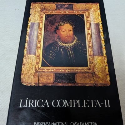 Capa de livro preto com retrato de Luís de Camões num quadro dourado e texto em branco.