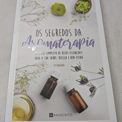 Capa de livro sobre aromaterapia com frascos e flores decorativas.