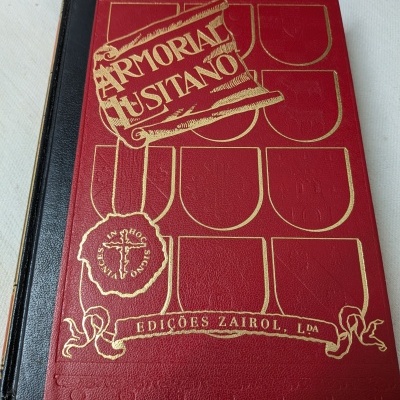 Livro capa dura vermelha e preta com brasões dourados e relevo