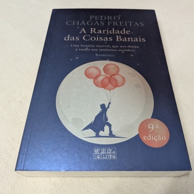 Capa de livro azul escuro com figura segurando balões vermelhos e lua branca, texto do título e edição