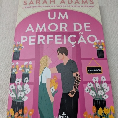 Capa de livro rosa com ilustração de casal e flores, texto em branco e rosa