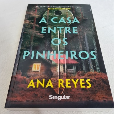 Livro 'A Casa Entre os Pinheiros' de Ana Reyes com imagem de casa em bosque