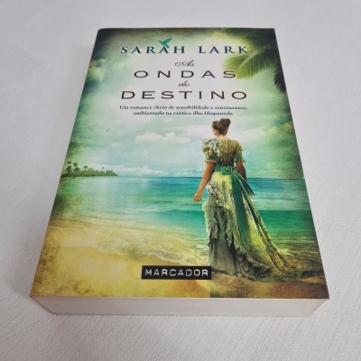 Livro 'As Ondas do Destino' de Sarah Lark com capa de mulher na praia