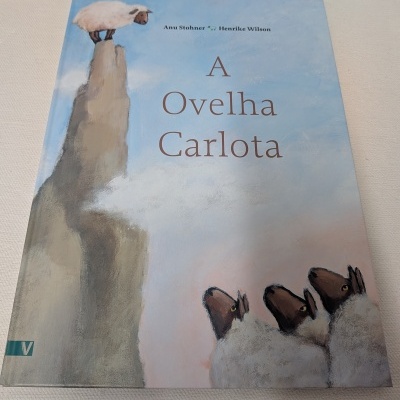 Capa de livro infantil A Ovelha Carlota com ilustração de ovelha em rocha e ovelhas olhando para cima