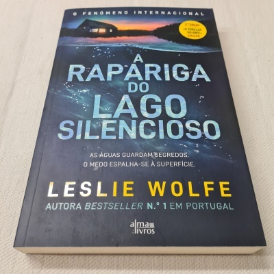 Capa do livro 'A rapariga do lago silencioso' de Leslie Wolfe, azul escuro com texto branco e amarelo