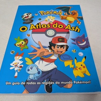 Livro 'Pokémon O Atlas do Ash' com personagens coloridos na capa e fundo azul