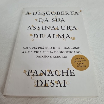 Livro com capa branca e letras pretas e douradas à vista, título e autor destacados
