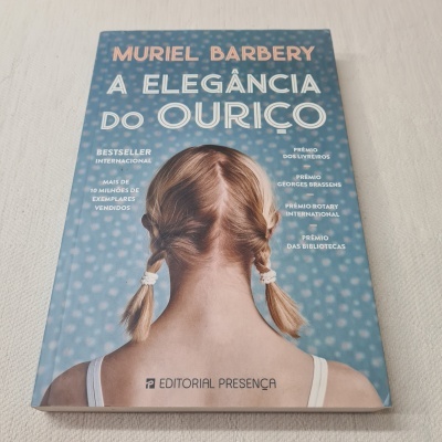 Livro 'A Elegância do Ouriço' com capa azul e imagem de jovem de costas com cabelo em tranças.