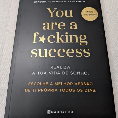 Capa de um livro preto com texto em dourado, branco e laranja.