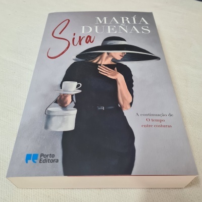 Capa do livro 'Sira' de María Dueñas com mulher vestida de preto e chapéu segurando chávena e bule brancos