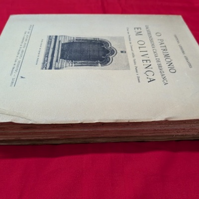 Livro antigo com capa amarela clara e texto preto sobre tecido vermelho