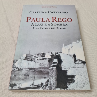 Capa de livro com imagem em preto e branco de caminho junto ao mar e título em letras vermelhas e pretas