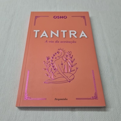 Capa de livro laranja com título 'TANTRA A via da aceitação' e ilustração de figura sentada entre plantas