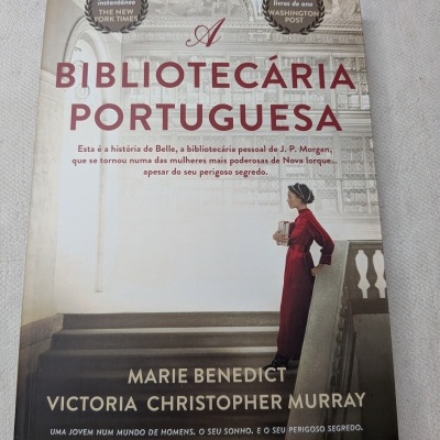 Capa do livro A Bibliotecária Portuguesa com mulher de vestido vermelho segurando livros junto a escada.
