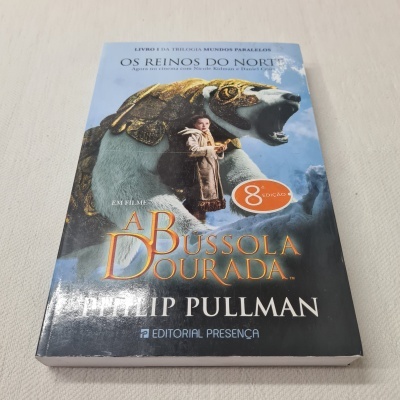 Capa do livro A Bussola Dourada com urso gigante e menina, texto e fundo azul