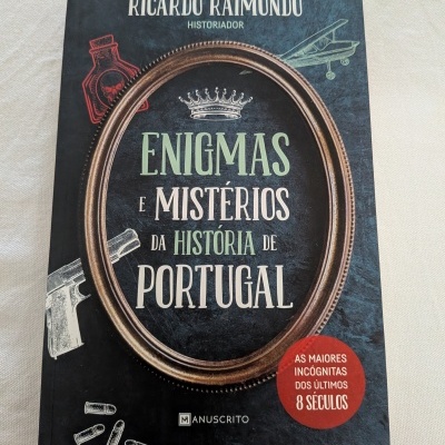 Livro Enigmas e Mistérios da História de Portugal com capa preta e moldura castanha oval