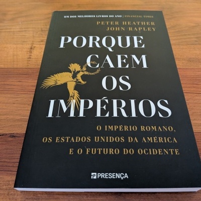 Livro Porque Caem os Impérios com capa preta e texto branco e dourado sobre mesa de madeira