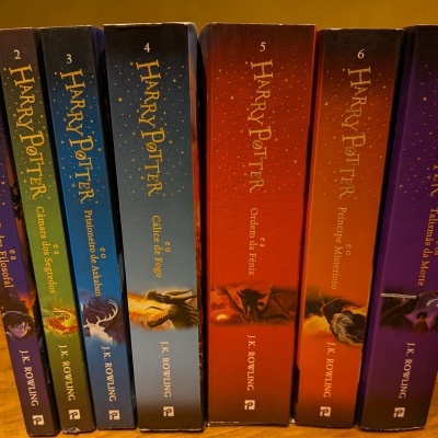 Sete livros de Harry Potter com capas coloridas alinhadas em superfície de madeira.