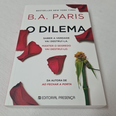 Capa de livro 'O Dilema' com pétalas de rosa vermelhas e uma rosa murcha verde