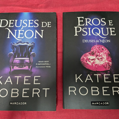 Dois livros Deuses de Néon e Eros e Psique de Katee Robert sobre tecido vermelho
