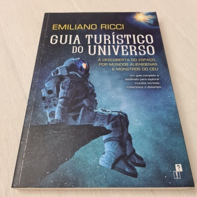 Livro 'Guia Turístico do Universo' com imagem de astronauta no espaço na capa