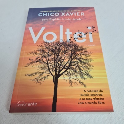 Livro Voltei de Chico Xavier com capa mostrando árvore e céu laranja