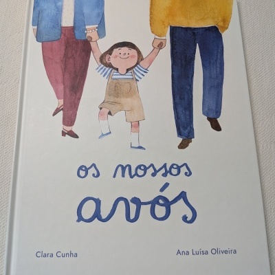 Capa de livro infantil com desenho de uma criança e dois adultos e texto os nossos avós.