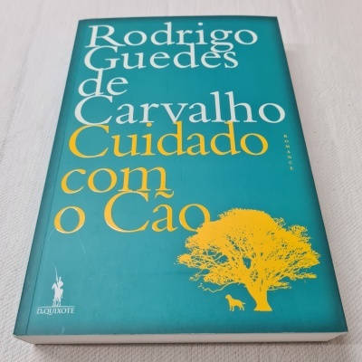 Capa de livro verde azulada com texto branco e amarelo e ilustração de árvore e cão