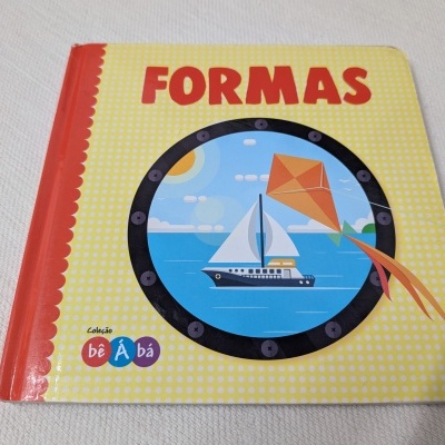 Capa de livro infantil amarelo com título FORMAS, barco e pipa, e texto Coleção bê Á bá