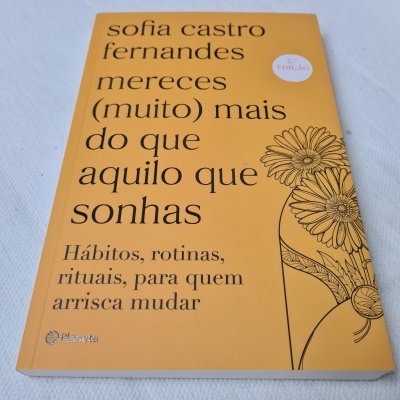 Livro com capa amarela com ilustração de flores e texto em preto, sobre uma superfície branca.
