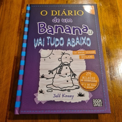 Capa de livro 'O Diário de um Banana 13 Vai Tudo Abaixo' de Jeff Kinney sobre mesa de madeira