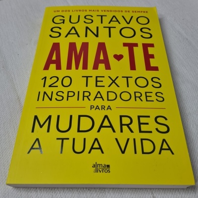 Livro amarelo de papel com texto inspirador de Gustavo Santos sobre superfície branca