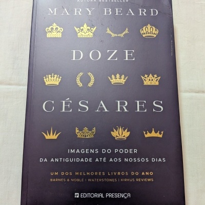 Capa de livro preto com coroas douradas e texto branco e dourado