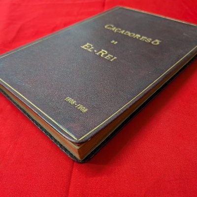 Livro velho de capa dura castanha sobre fundo vermelho.