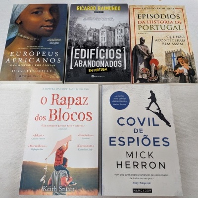 Cinco livros de capas variadas dispostos em superfície branca
