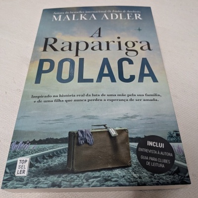 Capa de livro A Rapariga Polaca com mala castanha e lenço azul sobre trilhos de comboio