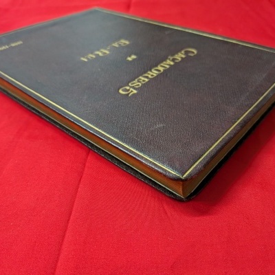 Livro com capa dura castanha e texto dourado sobre tecido vermelho