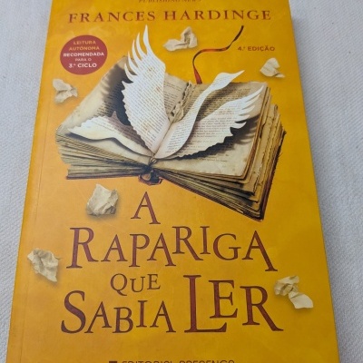 Capa do livro A Rapariga que Sabia Ler amarelo com ilustração de livro com asas