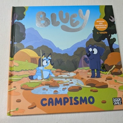 Capa de livro infantil Bluey Campismo com ilustração colorida de dois cães num acampamento.