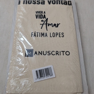 Livro com capa de tecido bege e texto a preto, embalado em plástico transparente