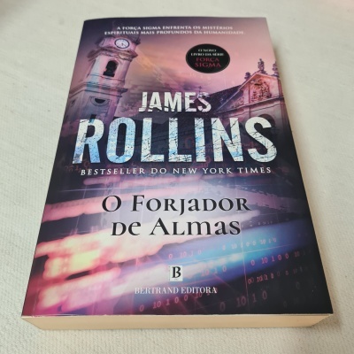 Livro 'O Forjador de Almas' de James Rollins com capa roxa e rosa mostrando um relógio de torre
