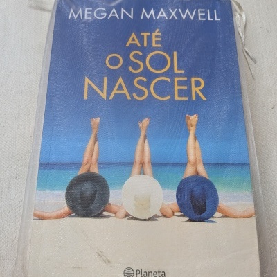 Livro Até o Sol Nascer de Megan Maxwell com capa azul e ilustração de pessoas na praia.
