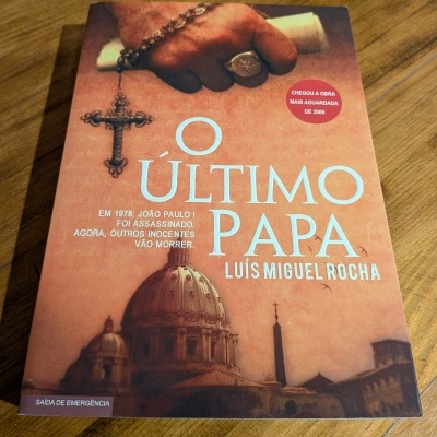 Capa do livro 'O Último Papa' com imagem de mão segurando rosário, cruz e Vaticano ao fundo