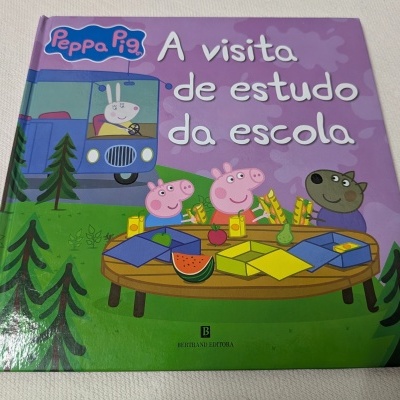 Capa de livro infantil Peppa Pig com título e personagens à volta de mesa ao ar livre