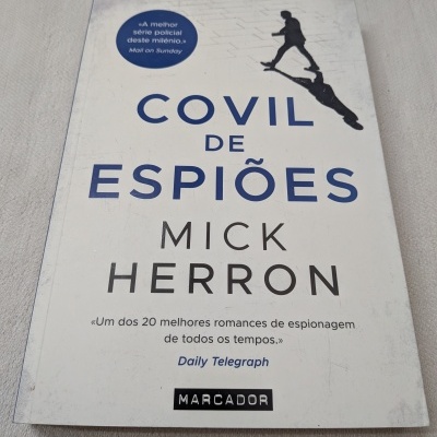 Capa de livro Covil de Espiões de Mick Herron com fundo branco e texto azul e preto