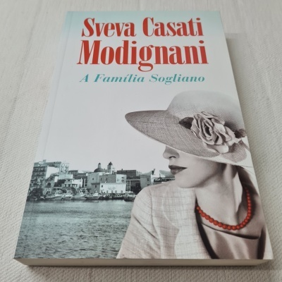 Livro 'A Família Sogliano' de Sveva Casati Modignani com capa de mulher elegante e cidade costeira